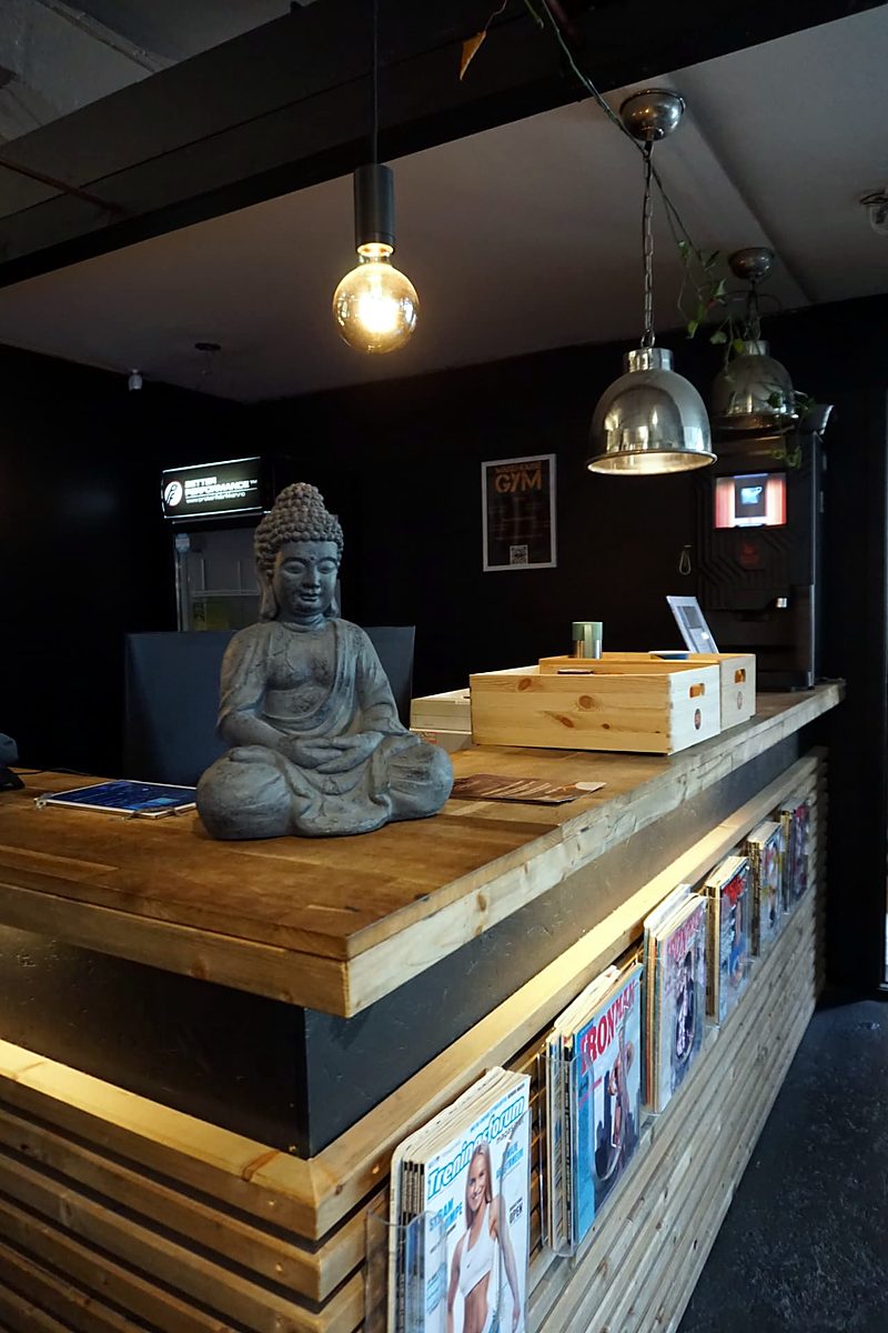 Resepsjonsdisk i treverk med en sittende Buddha-statue, magasinholdere og industrilamper